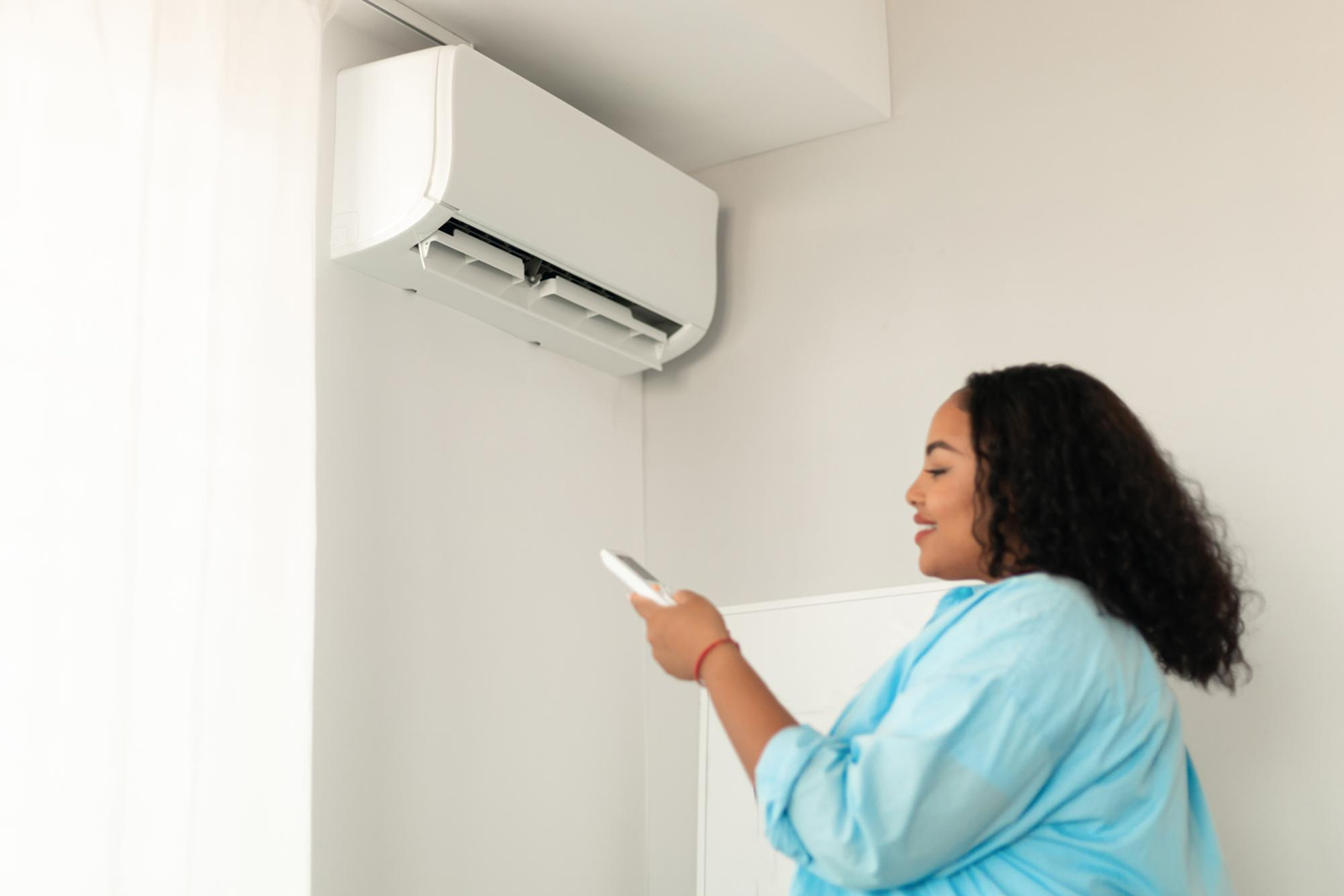 Woman adjusting a wall-mounted air conditioner with a remote control