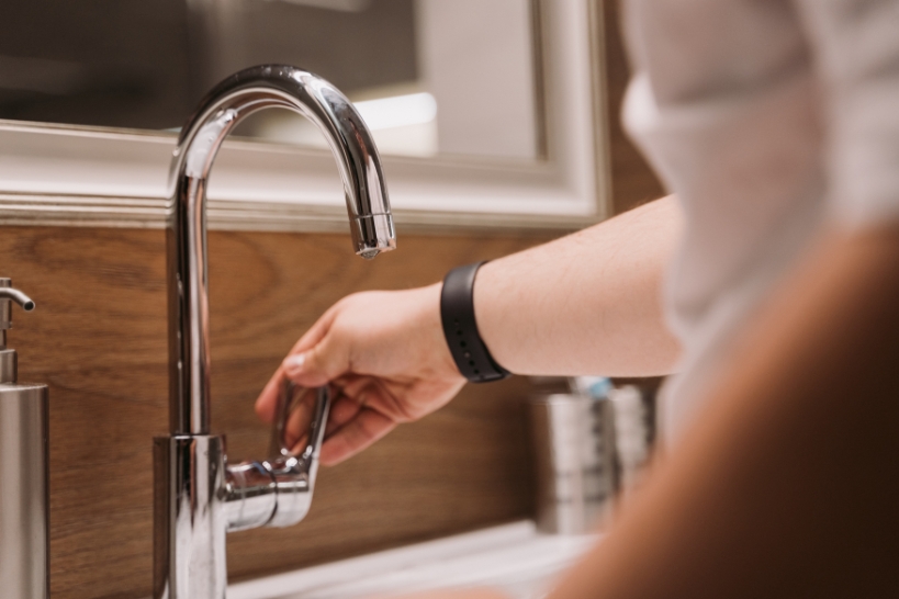 Homeowner testing a bathroom faucet for rising water or gurgling that may indicate a sewer line problem.