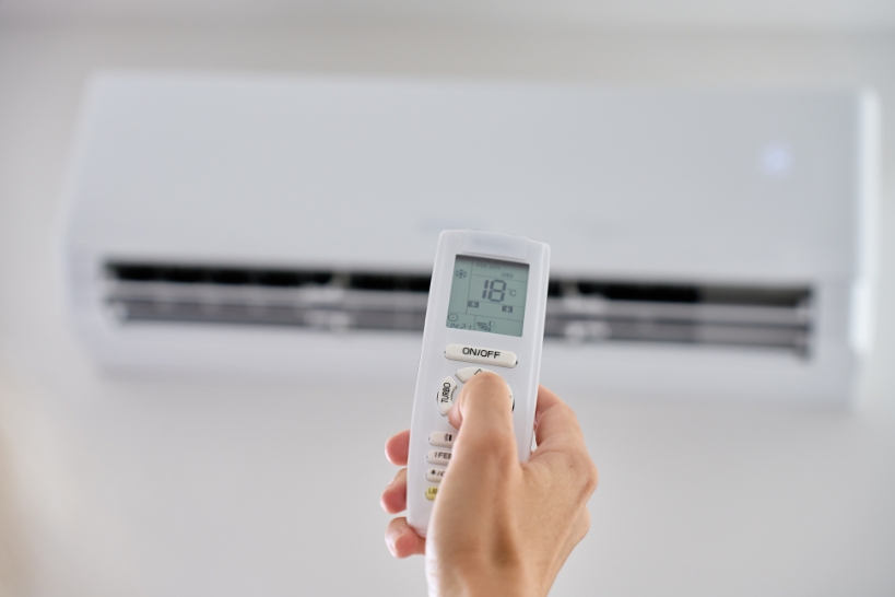 Person checking thermostat mode and fan settings on a ductless mini-split remote control.