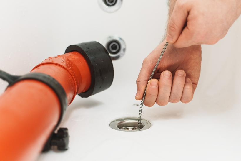Person using a drain snake and plunger to clear a clogged sink drain.