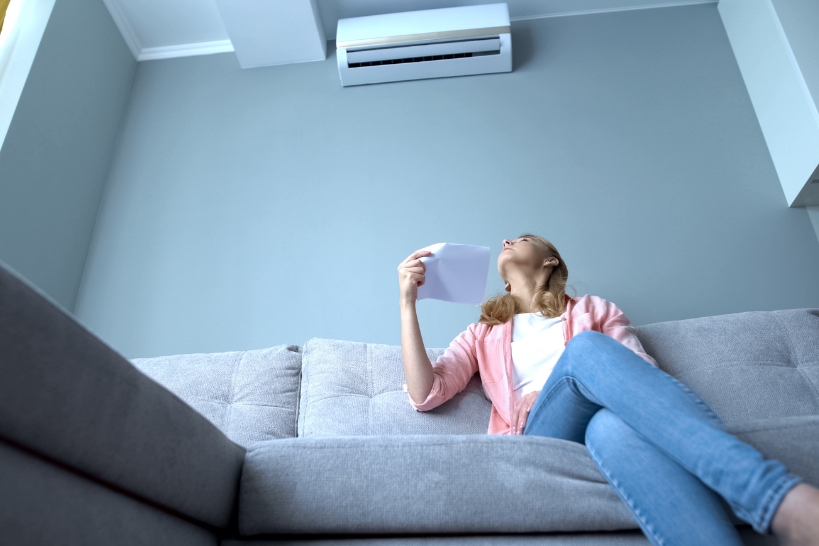 Woman feeling uncomfortable indoors due to high humidity and sticky air while the air conditioner is running.
