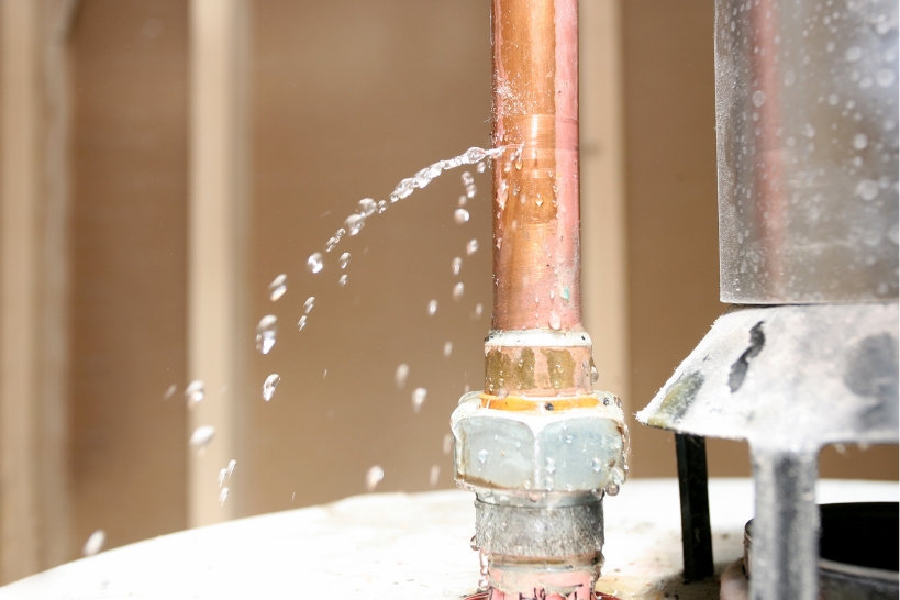 Water spraying from a leaking copper pipe connection near a residential water heater.