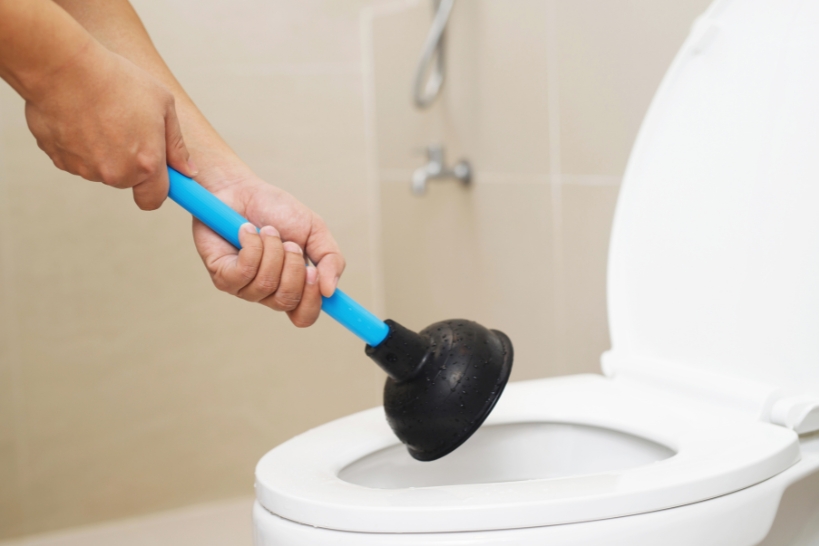 Homeowner repeatedly using a plunger on a slow-flushing toilet, a possible sign of a sewer line problem.
