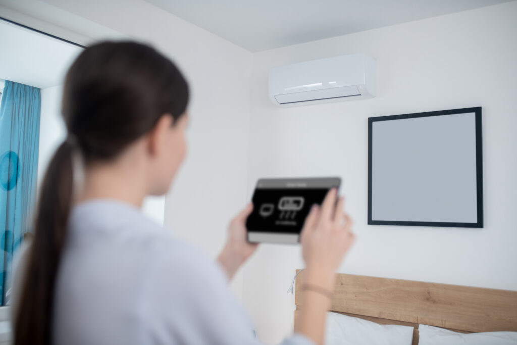 Woman using a tablet to control a wall-mounted ductless mini-split air conditioner.